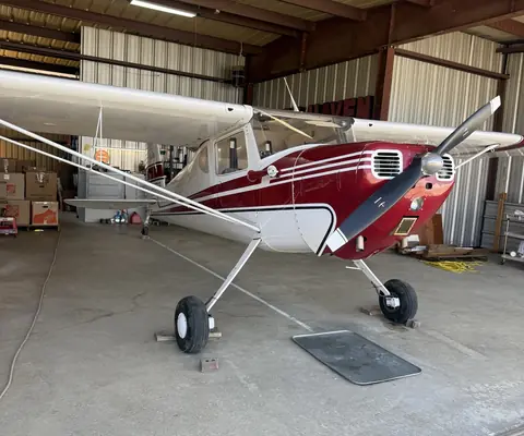 A red and white vintage Cessna taildragger parked inside a hangar