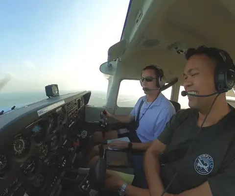 Instructor and student side by side in the cockpit, headsets on, in flight