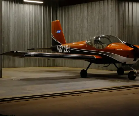 N812EJ, an orange Van's RV-12iS, parked in a lit hangar at dusk