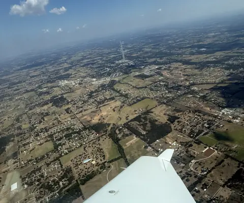 Looking down past a white low wing at farmland and small towns from cruising altitude