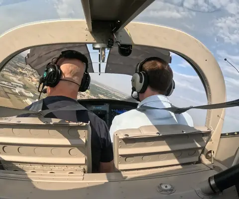 Instructor and student in the RV-12 cockpit, headsets on, with the city below the canopy